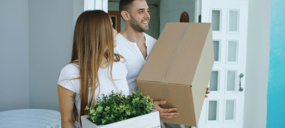 Couple carrying moving boxes into a new home