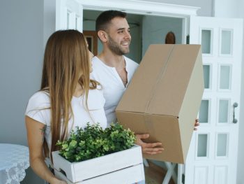 Couple carrying moving boxes into a new home
